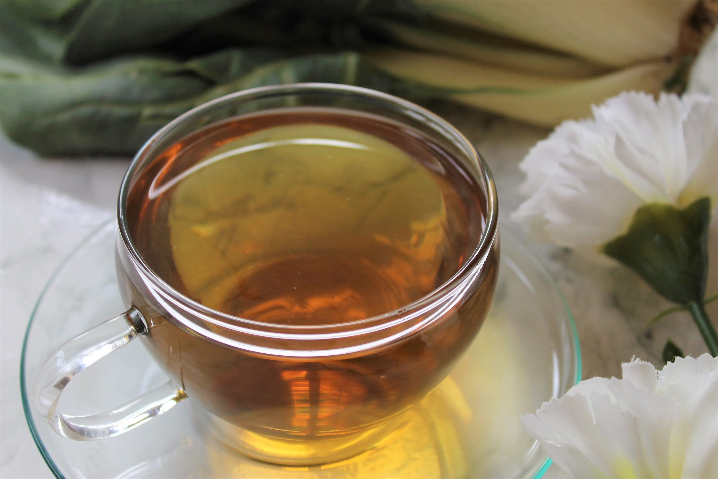 gold coloured tea in glass teacup with white flowers