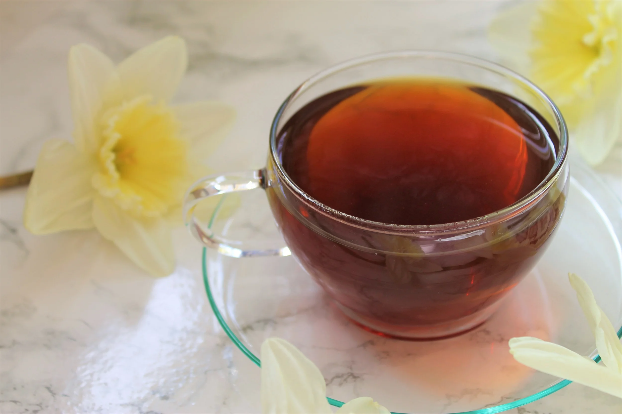 black tea in glass teacup surrounded by daffodils